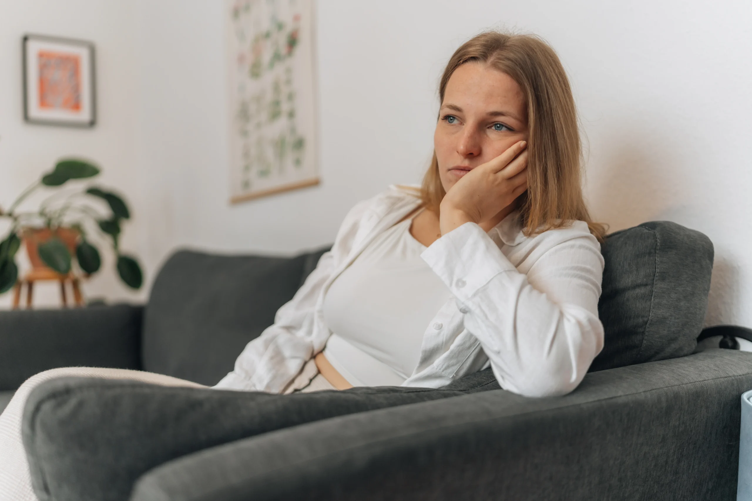 Frau sitzt erschöpft und nachdenklich auf dem Sofa, belastet von Neurodermitis