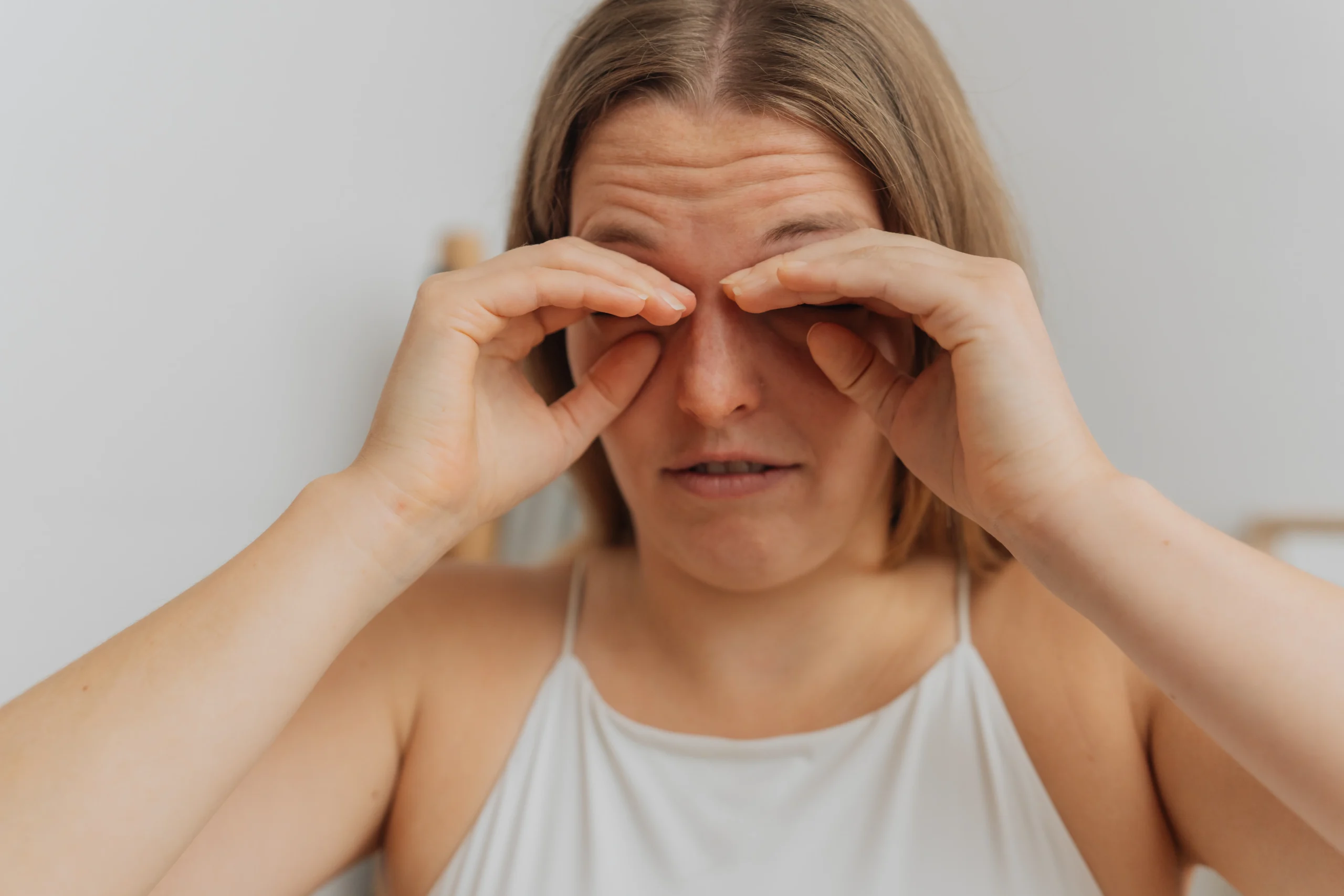 Frau reibt sich mit beiden Händen die geschlossenen Augen, Stirn in Falten gelegt – Symbolbild für Neurodermitis am Auge