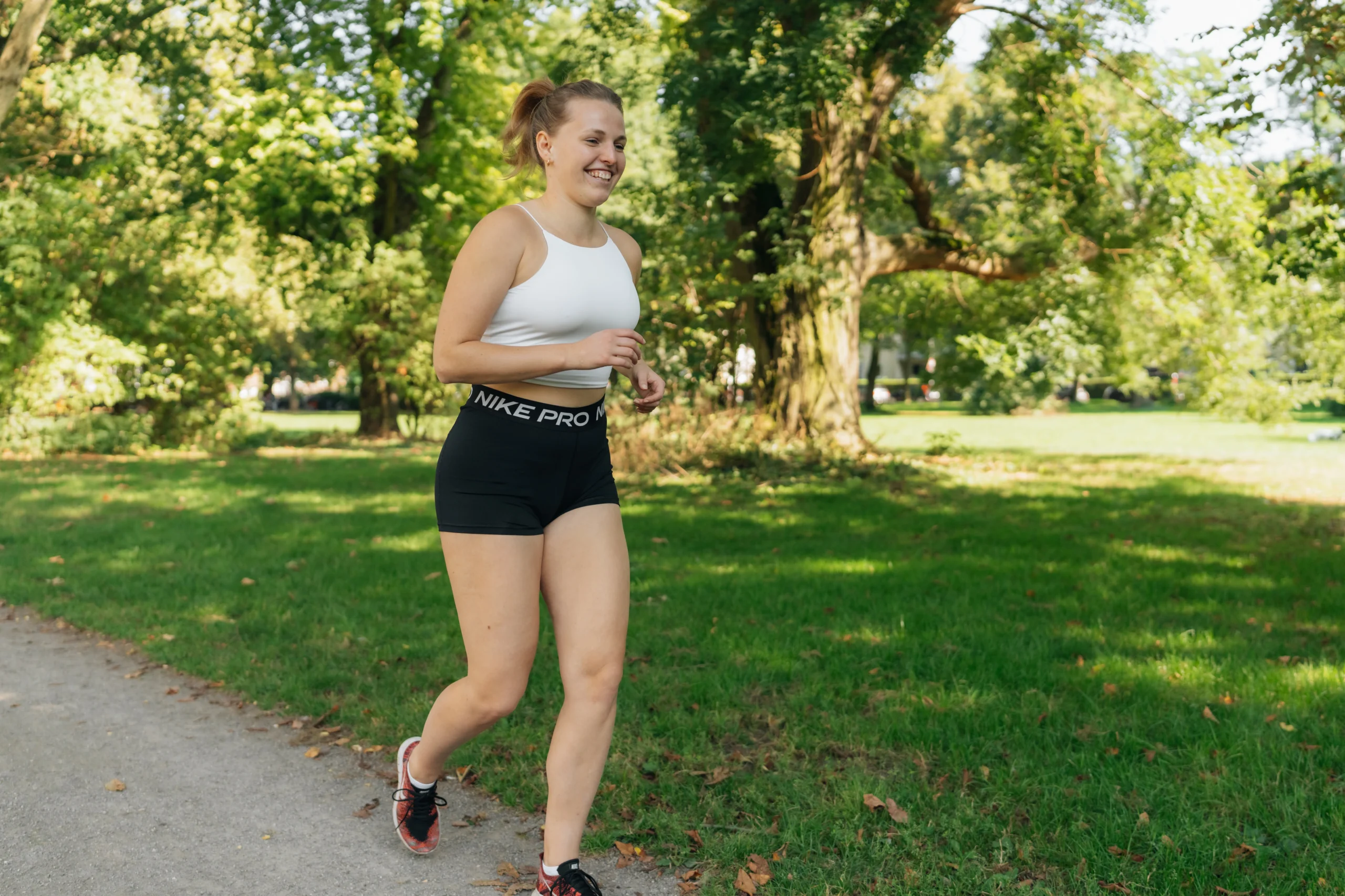 Lächelnde Frau joggt in Sportkleidung auf einem Parkweg, freie Beinbewegung ohne sichtbare Einschränkung – Symbolbild für Neurodermitis am Knie