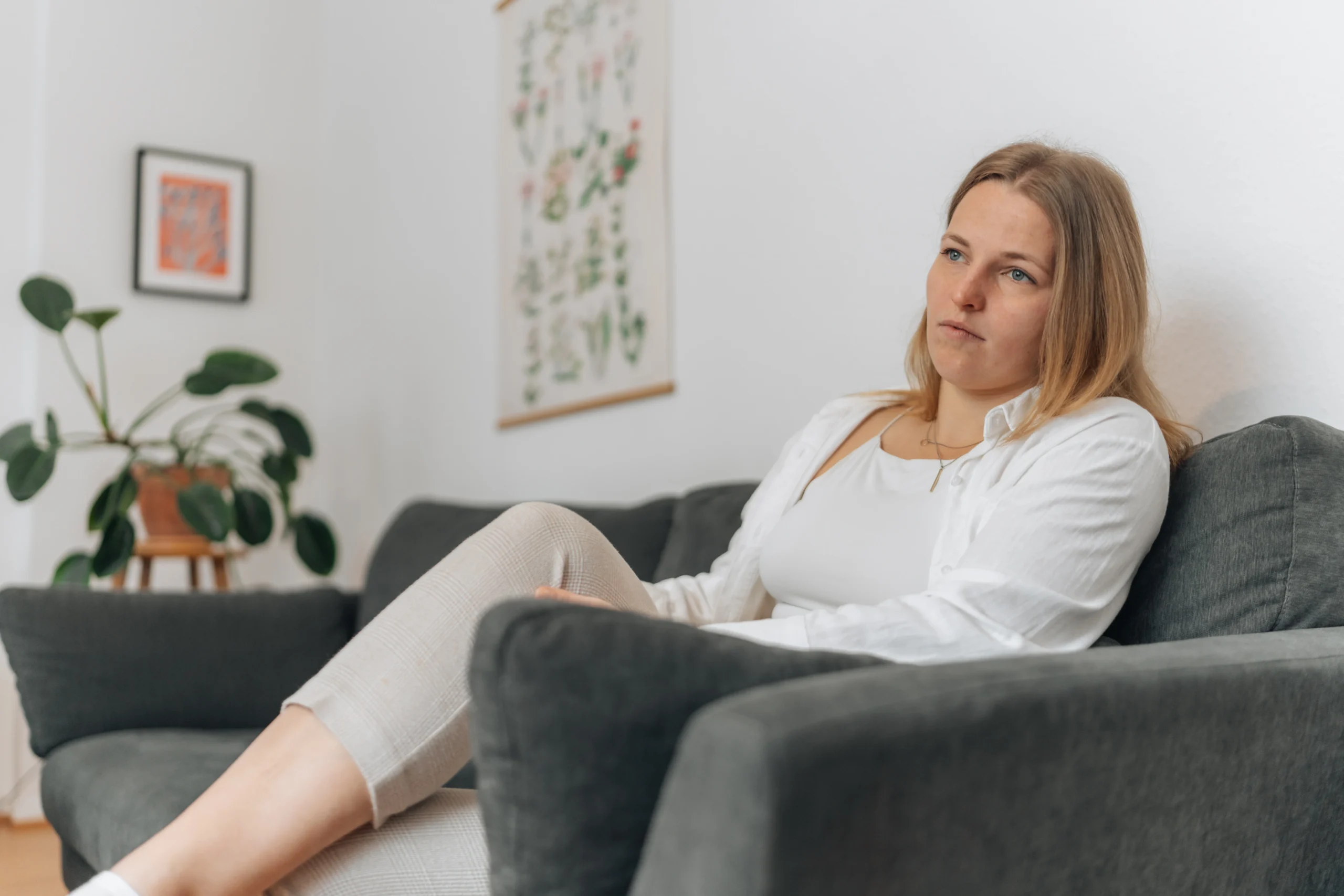 Frau sitzt nachdenklich mit hochgelegten Beinen auf dem Sofa