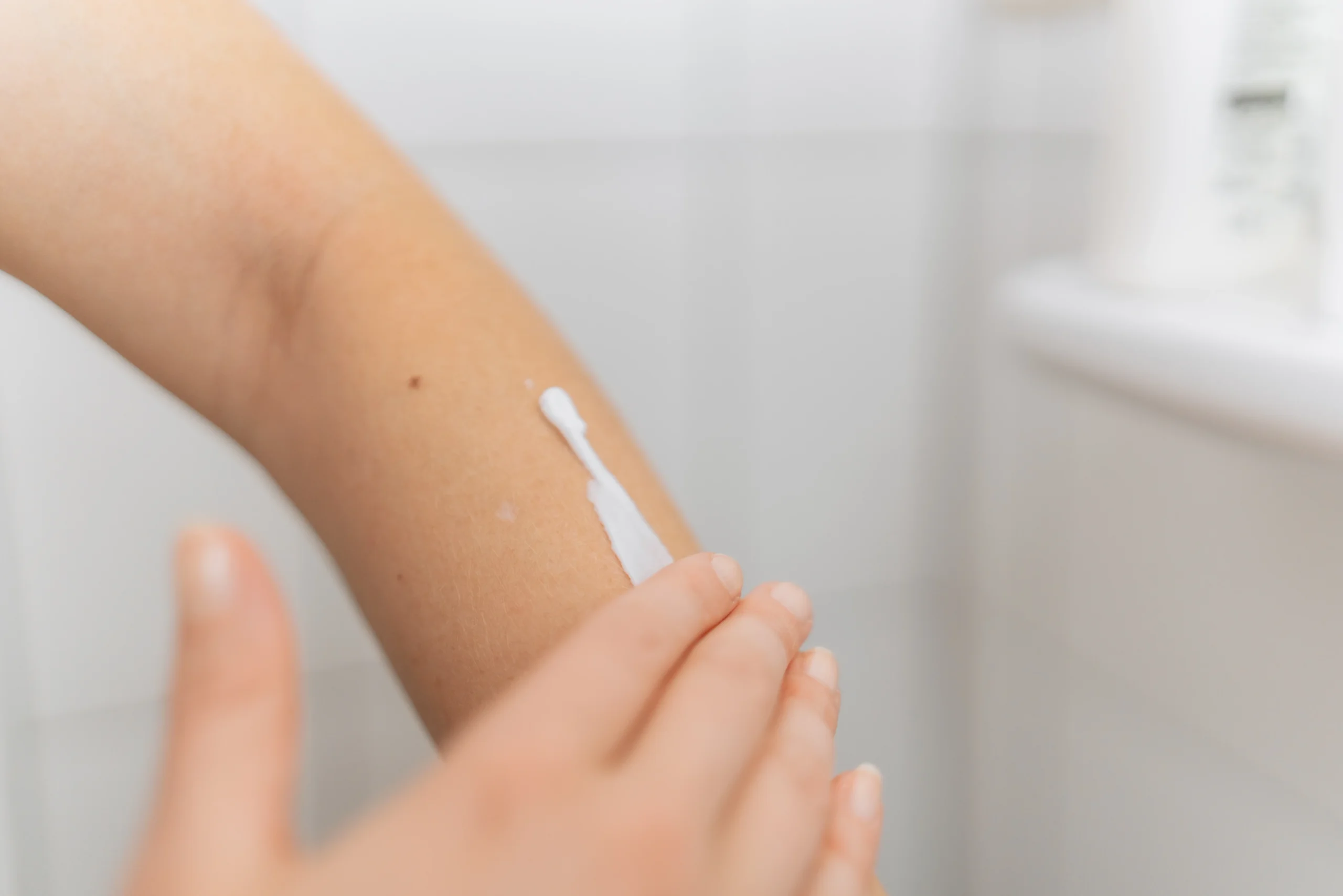 Hand verteilt eine weiße Creme auf einem Unterarm
