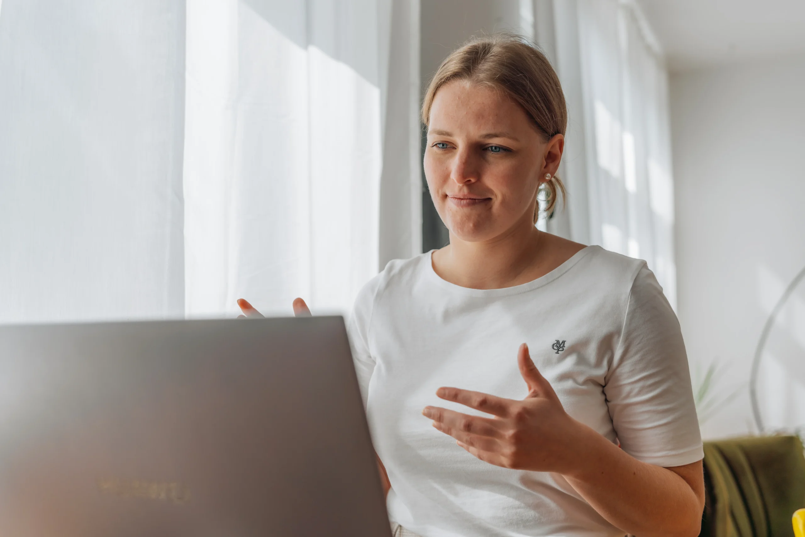 Junge Frau sitzt vor einem Laptop und spricht gestikulierend in einem Videogespräch