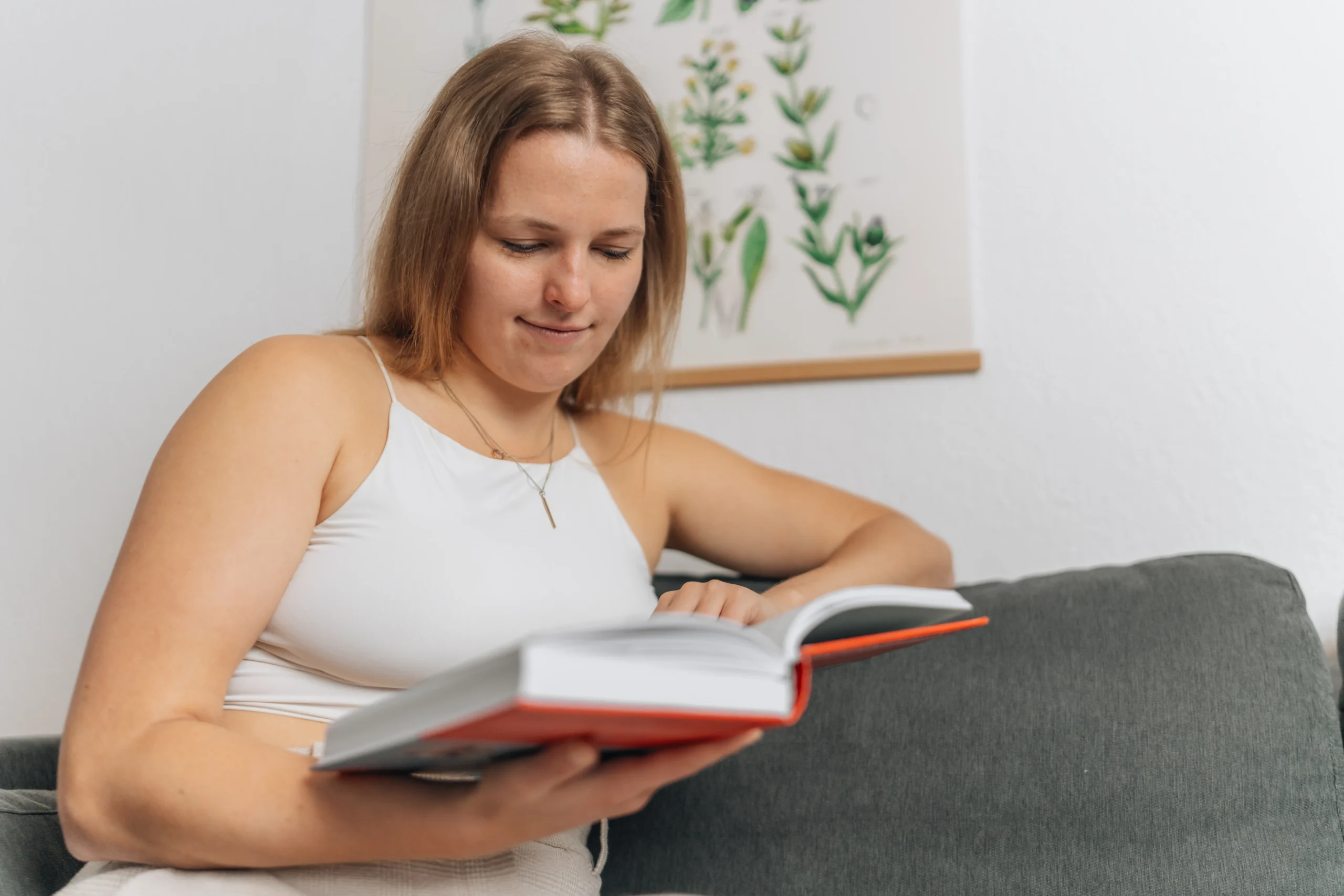 Eine junge Frau sitzt entspannt auf dem Sofa und liest konzentriert in einem Buch
