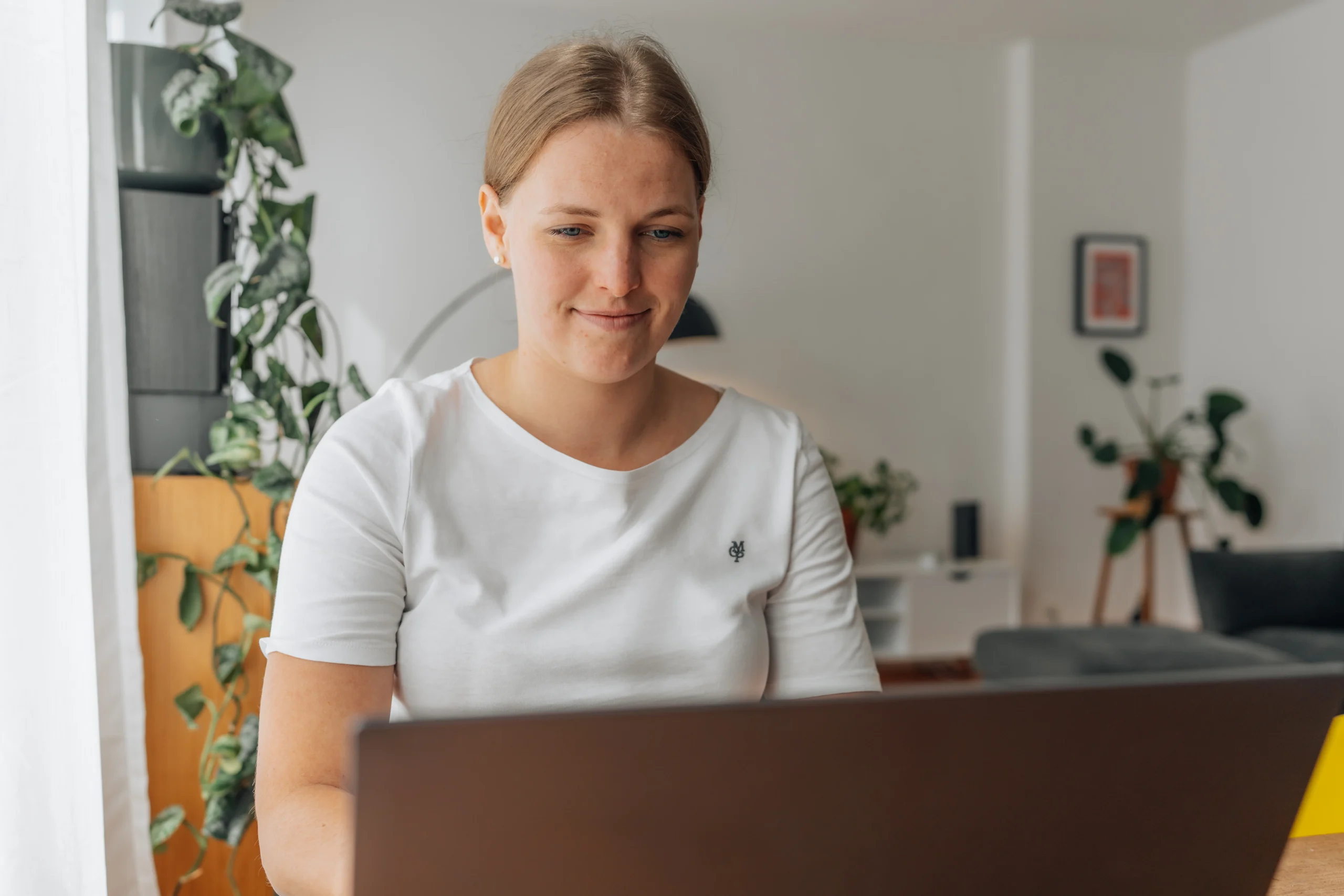 Junge Frau sitzt mit lächelndem Gesichtsausdruck vor einem Laptop und arbeitet konzentriert