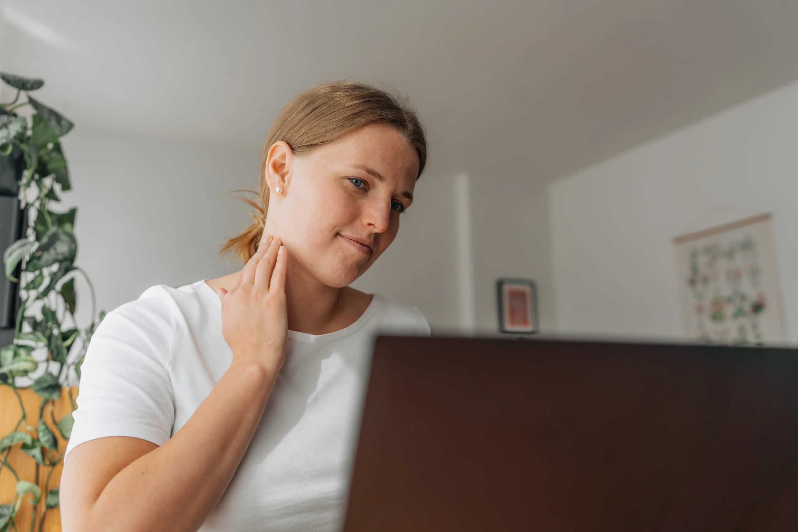 Frau kratzt sich am Hals, während sie am Laptop sitzt